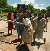 Children pump water. A sign in the background says 'drilled using funds from fairtrade'